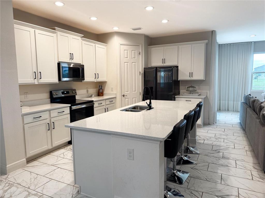 A modern kitchen features white cabinets, a large quartz island, and marble-look tile flooring — 5052 CENTER COURT, ST CLOUD, FL