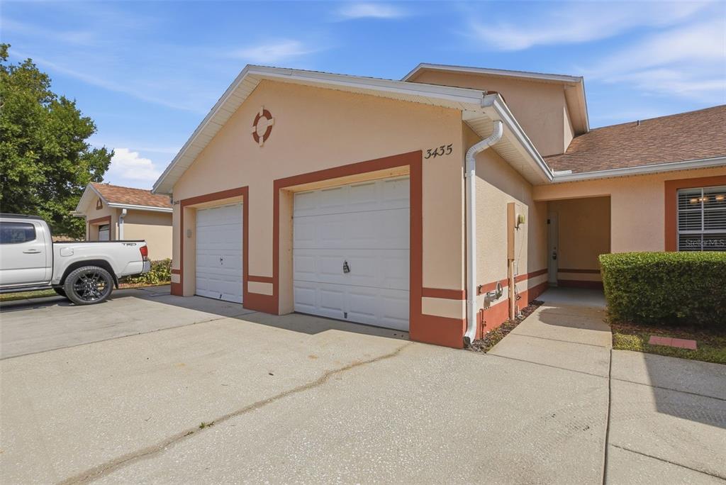 A tan duplex exterior features two white garage doors and a concrete driveway — 3435 VILLAGE GREEN COURT, ST CLOUD, FL