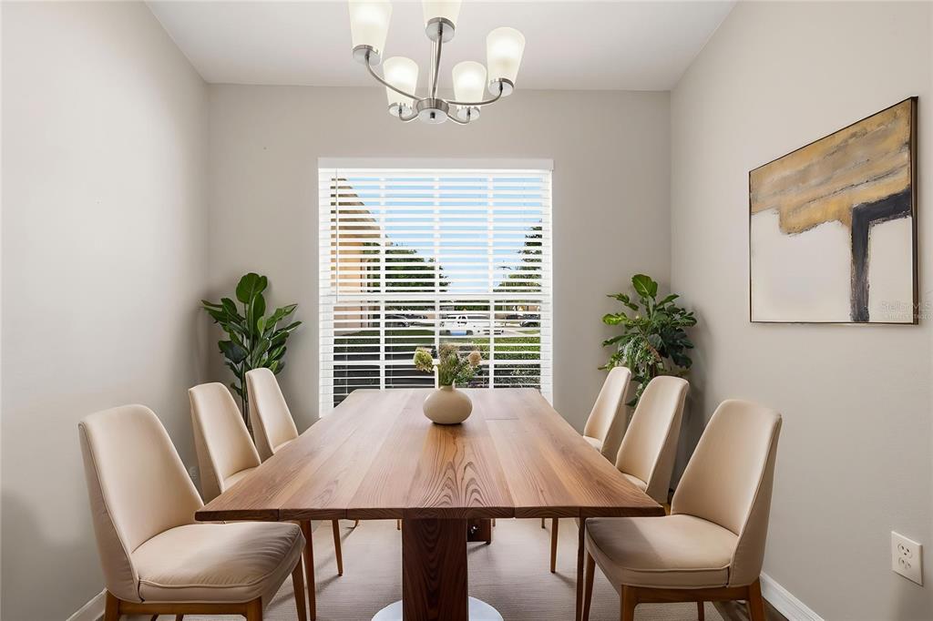 A dining room features a wooden table, six beige chairs, a chandelier, and a window — 3435 VILLAGE GREEN COURT, ST CLOUD, FL