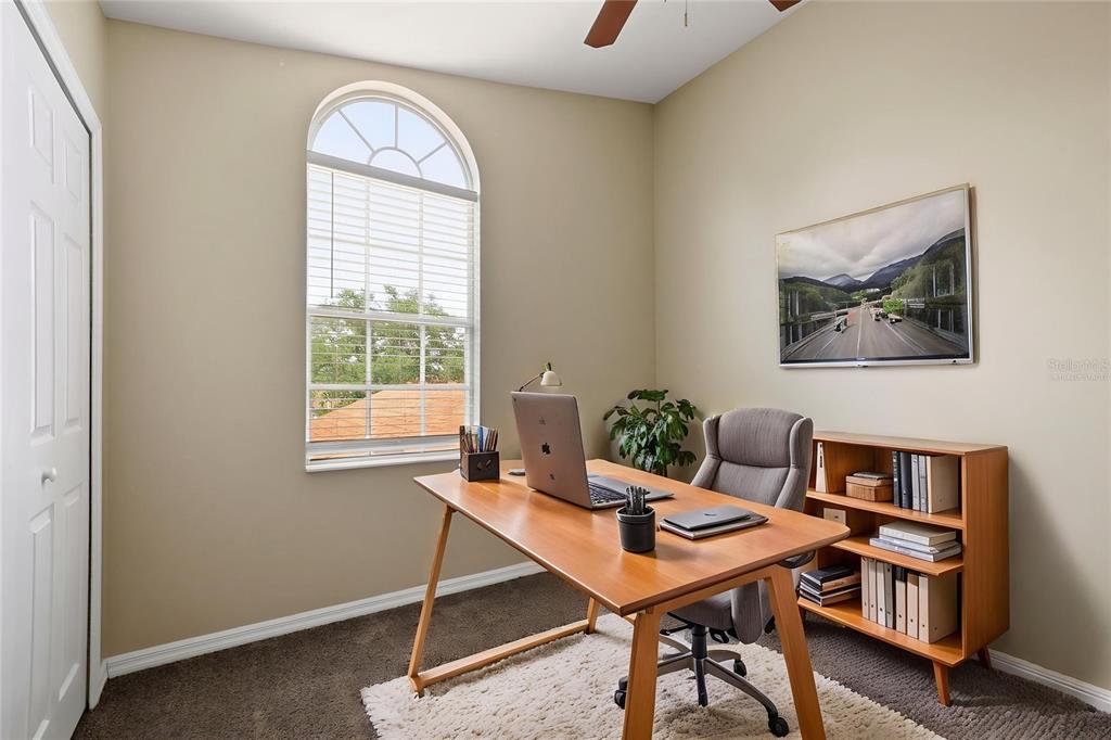 A home office features a wooden desk, a gray chair, a bookshelf, and an arched window — 3435 VILLAGE GREEN COURT, ST CLOUD, FL