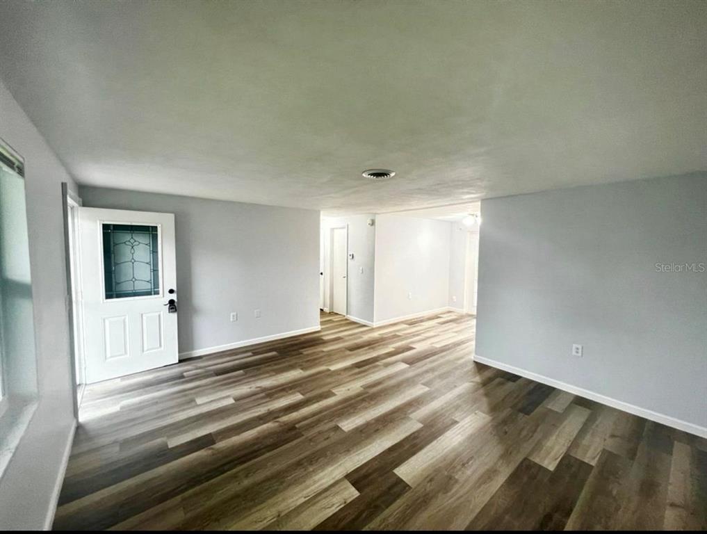 An empty living room features light gray walls, wood-look flooring, and a white front door — 3331 MONTICELLO STREET, HOLIDAY, FL
