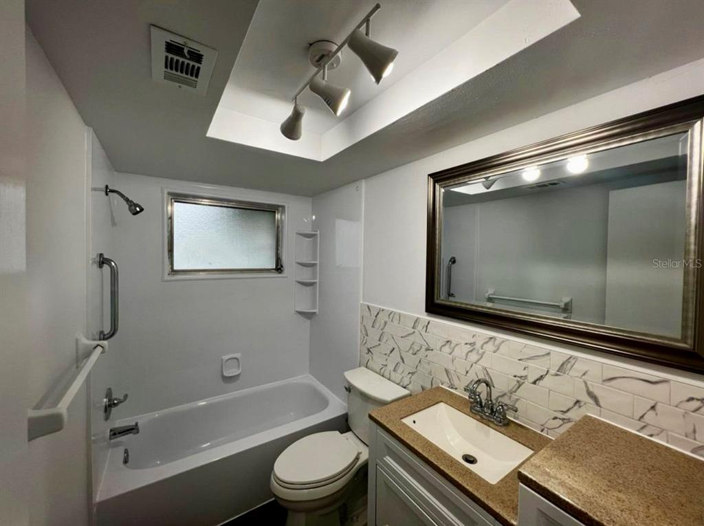 A bathroom features a white bathtub, a toilet, and a vanity with a marble-patterned backsplash — 3331 MONTICELLO STREET, HOLIDAY, FL