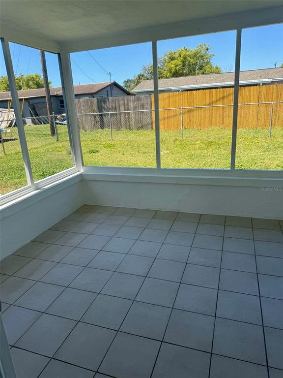A sunroom with white tiled flooring, white walls, and large windows overlooking a fenced backyard — 3331 MONTICELLO STREET, HOLIDAY, FL