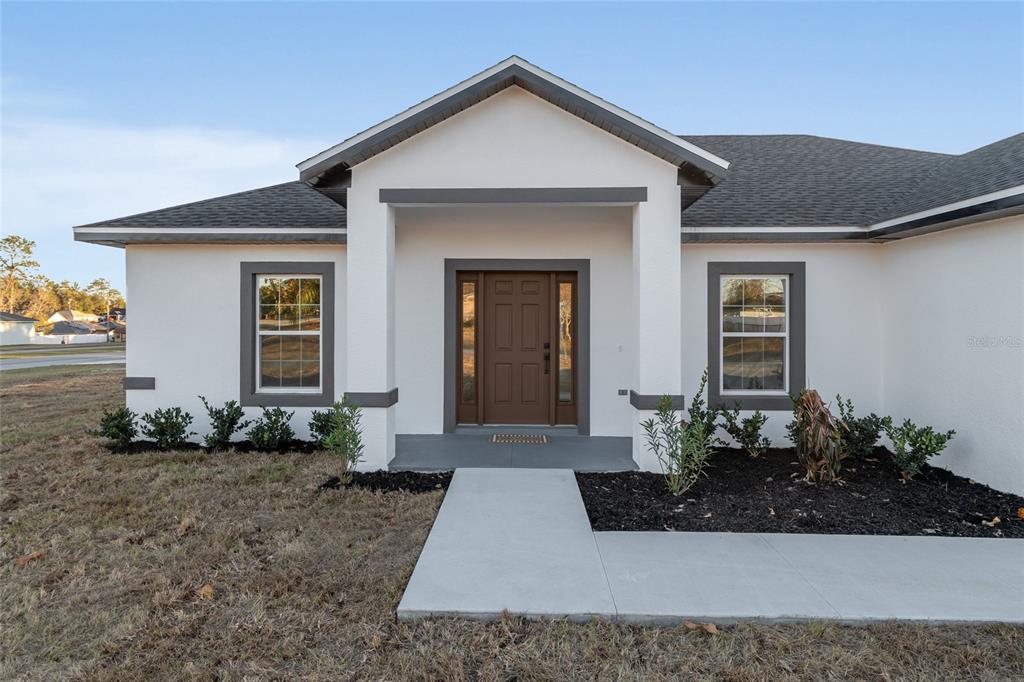 The exterior of a white house features a covered entryway, a brown door, and landscaping — 4612 SW 149TH STREET, OCALA, FL