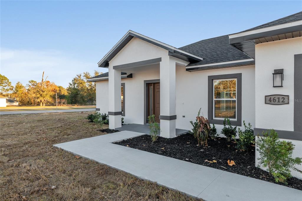 A white stucco house exterior features a covered entryway, dark trim, and a concrete walkway — 4612 SW 149TH STREET, OCALA, FL