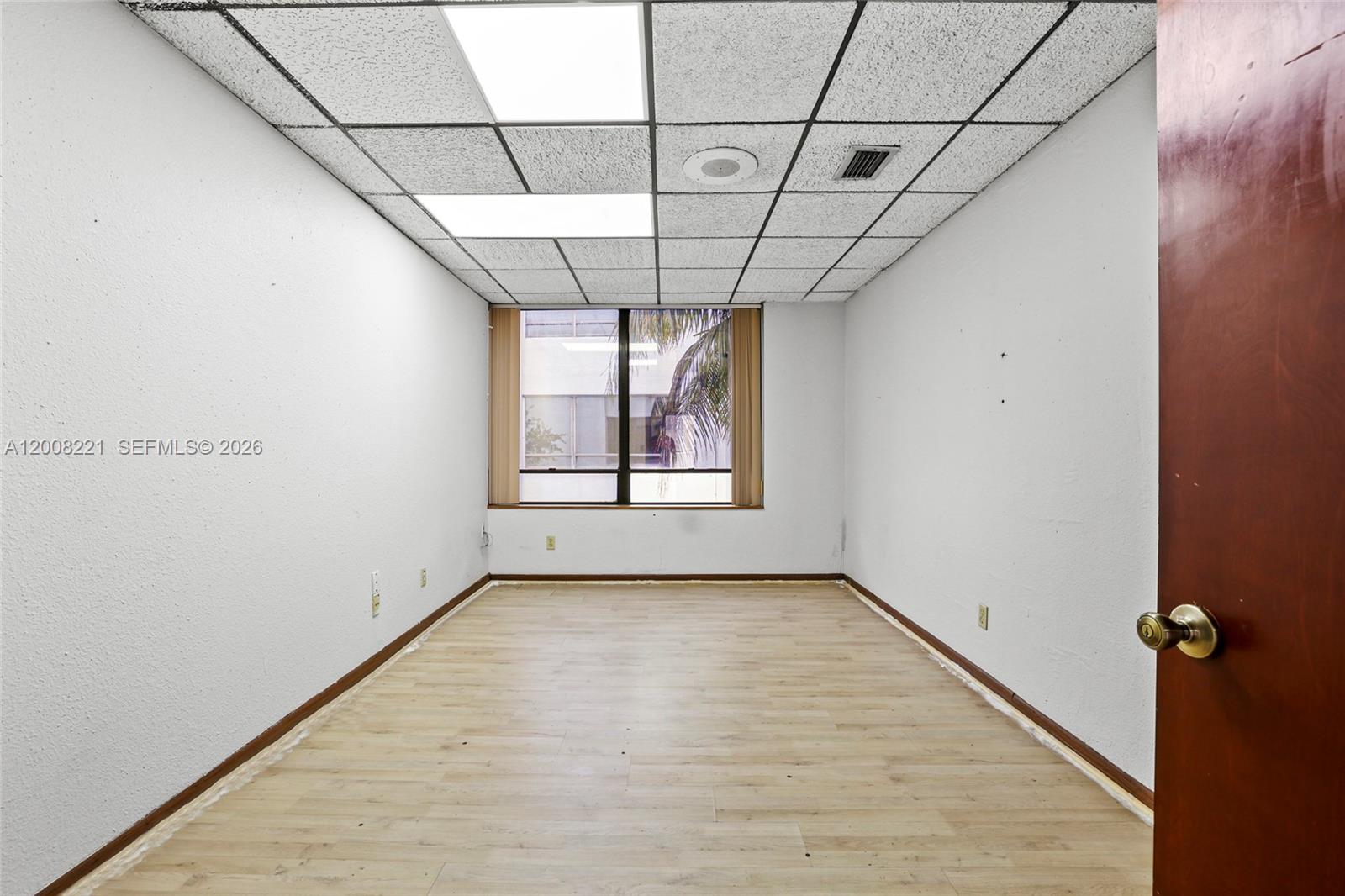 An empty office room features a drop ceiling, light wood flooring, and a window view — 8358 W Oakland Park Blvd # A, Sunrise FL 33351, SUNRISE, FL