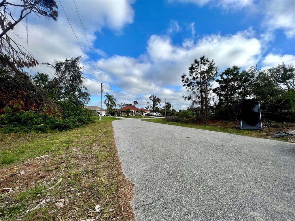 A paved road leads toward houses surrounded by trees under a partly cloudy sky — LOT 9 BRADDOCK AVENUE, NORTH PORT, FL