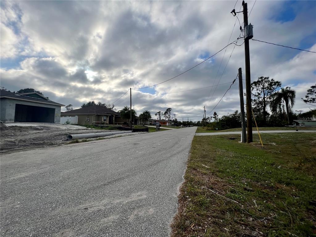 A paved residential street features utility poles, a new house under construction, and cloudy skies — LOT 9 BRADDOCK AVENUE, NORTH PORT, FL