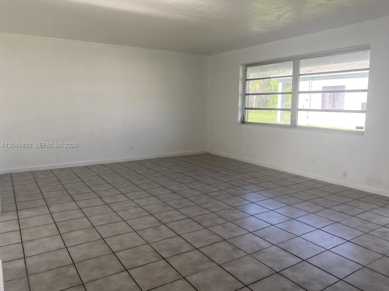 An empty room features white walls, large windows, and light-colored square floor tiles — 5904 SW 27th St, West Park FL 33023, WEST PARK, FL