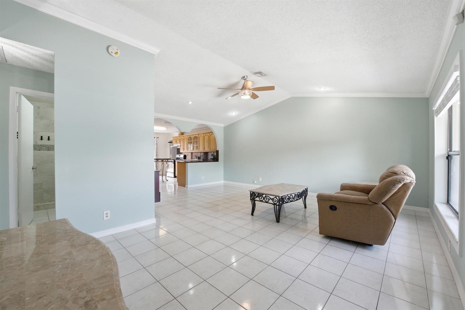 A spacious living room with light blue walls, white tile flooring, and a ceiling fan — 5814 Ithaca Circle E, Lake Worth FL 33463, LAKE WORTH, FL