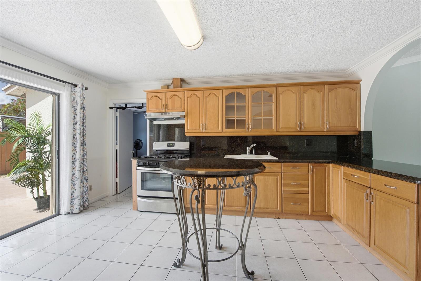 A kitchen features light wood cabinets, dark granite countertops, white tile flooring, and a sliding door — 5814 Ithaca Circle E, Lake Worth FL 33463, LAKE WORTH, FL