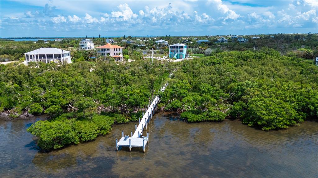 An aerial view shows a long wooden dock extending from a lush, tree-covered shoreline — 180 HORSESHOE LOOP ROAD, TERRA CEIA, FL