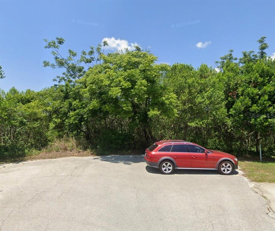 A red station wagon is parked on a paved lot in front of dense trees — 1712 ANSLEY COURT, DELTONA, FL