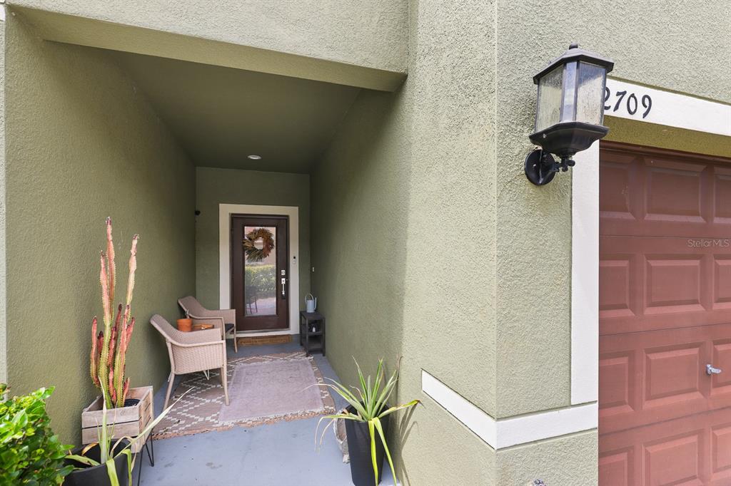 A covered entryway features a front door, two wicker chairs, and potted plants — 2709 ISABELLA VALLEY COURT, BRANDON, FL