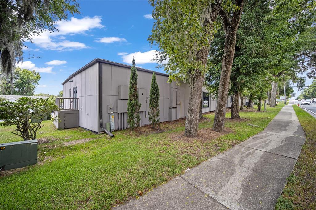 The exterior of a gray, single-story commercial building sits next to a sidewalk and trees — 2300 SE 17TH STREET UNIT 1100, OCALA, FL