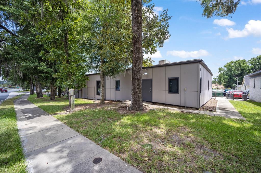 A single-story modular building with gray siding stands next to a sidewalk and trees — 2300 SE 17TH STREET UNIT 1100, OCALA, FL