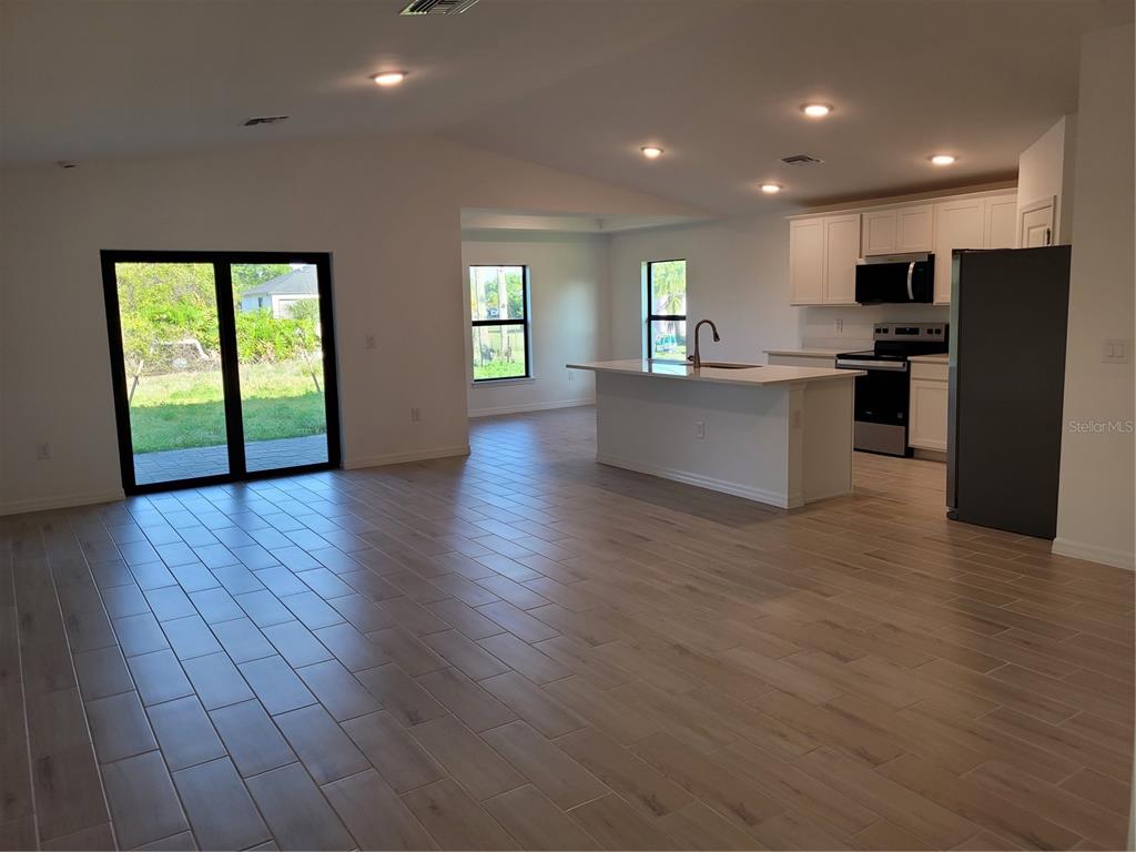 An open-concept kitchen and living area features light wood-look tile flooring and white cabinetry — 6305 SHAW STREET, ENGLEWOOD, FL