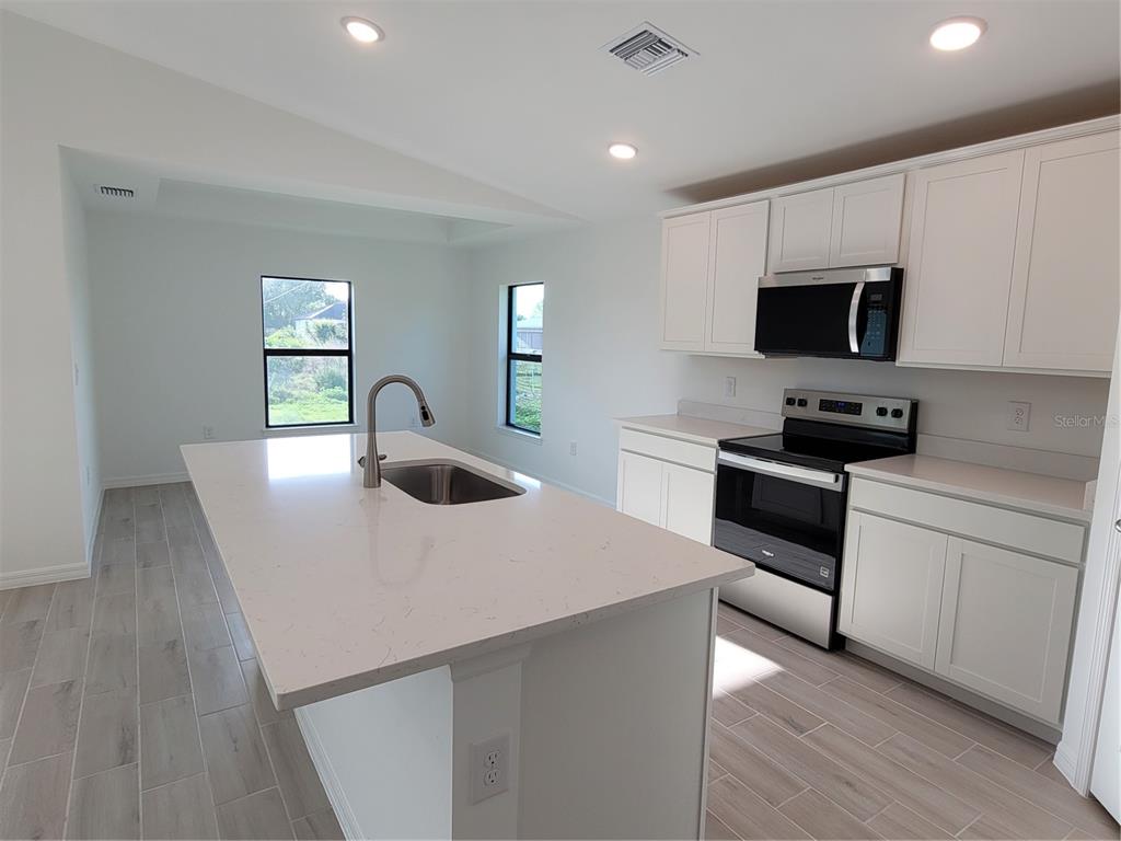 A modern kitchen features white cabinets, a quartz island with a sink, and light flooring — 6305 SHAW STREET, ENGLEWOOD, FL