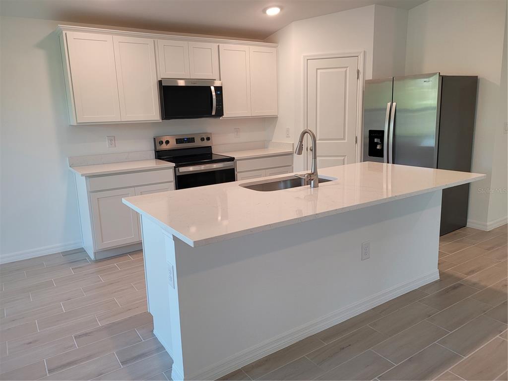 A kitchen features white cabinets, stainless steel appliances, a quartz island, and light tile flooring — 6305 SHAW STREET, ENGLEWOOD, FL