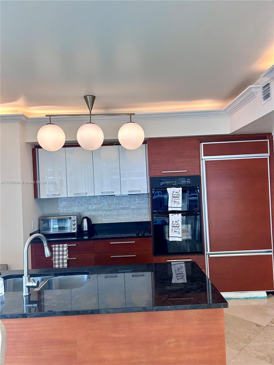 A kitchen features dark wood cabinetry, a black granite island, and a three-globe pendant light — 1830 S Ocean Dr # 4106, Hallandale Beach FL 33009, HALLANDALE BEACH, FL