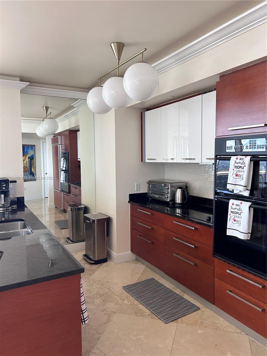 A kitchen features wood and white cabinetry, black countertops, and a three-globe pendant light — 1830 S Ocean Dr # 4106, Hallandale Beach FL 33009, HALLANDALE BEACH, FL