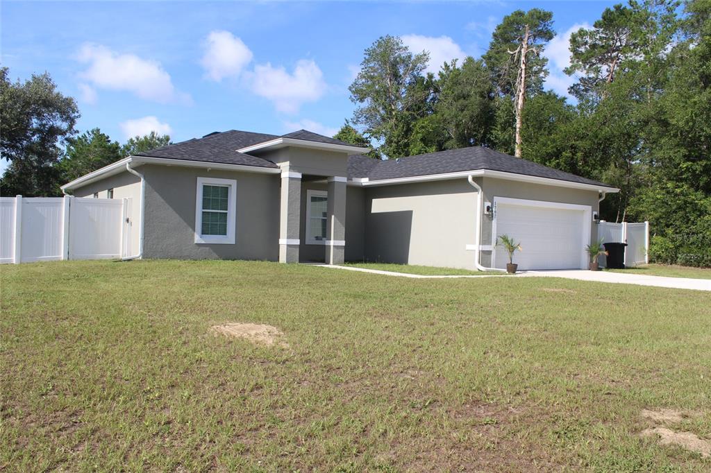 A single-story house with a gray stucco exterior, a two-car garage, and white fencing — 1787 SW 168TH LOOP, OCALA, FL