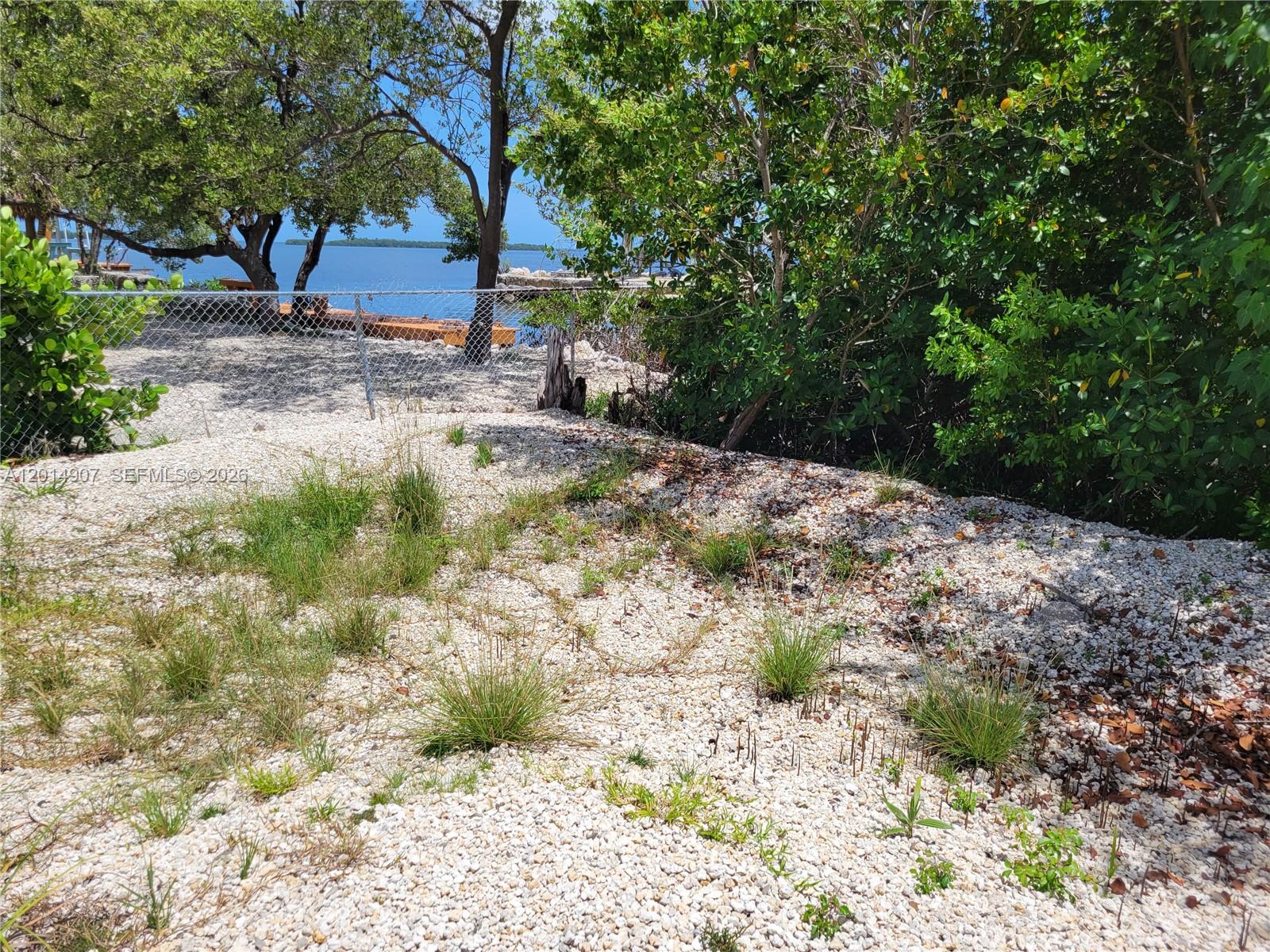 A gravel-covered yard leads to a chain-link fence overlooking a body of water — 799 Hazel St # 799, Key Largo FL 33037, KEY LARGO, FL