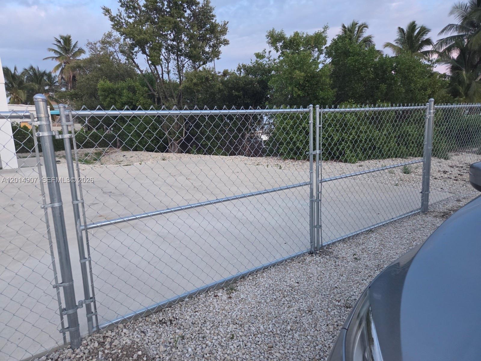 A chain-link fence encloses a concrete lot with trees and gravel in the background — 799 Hazel St # 799, Key Largo FL 33037, KEY LARGO, FL