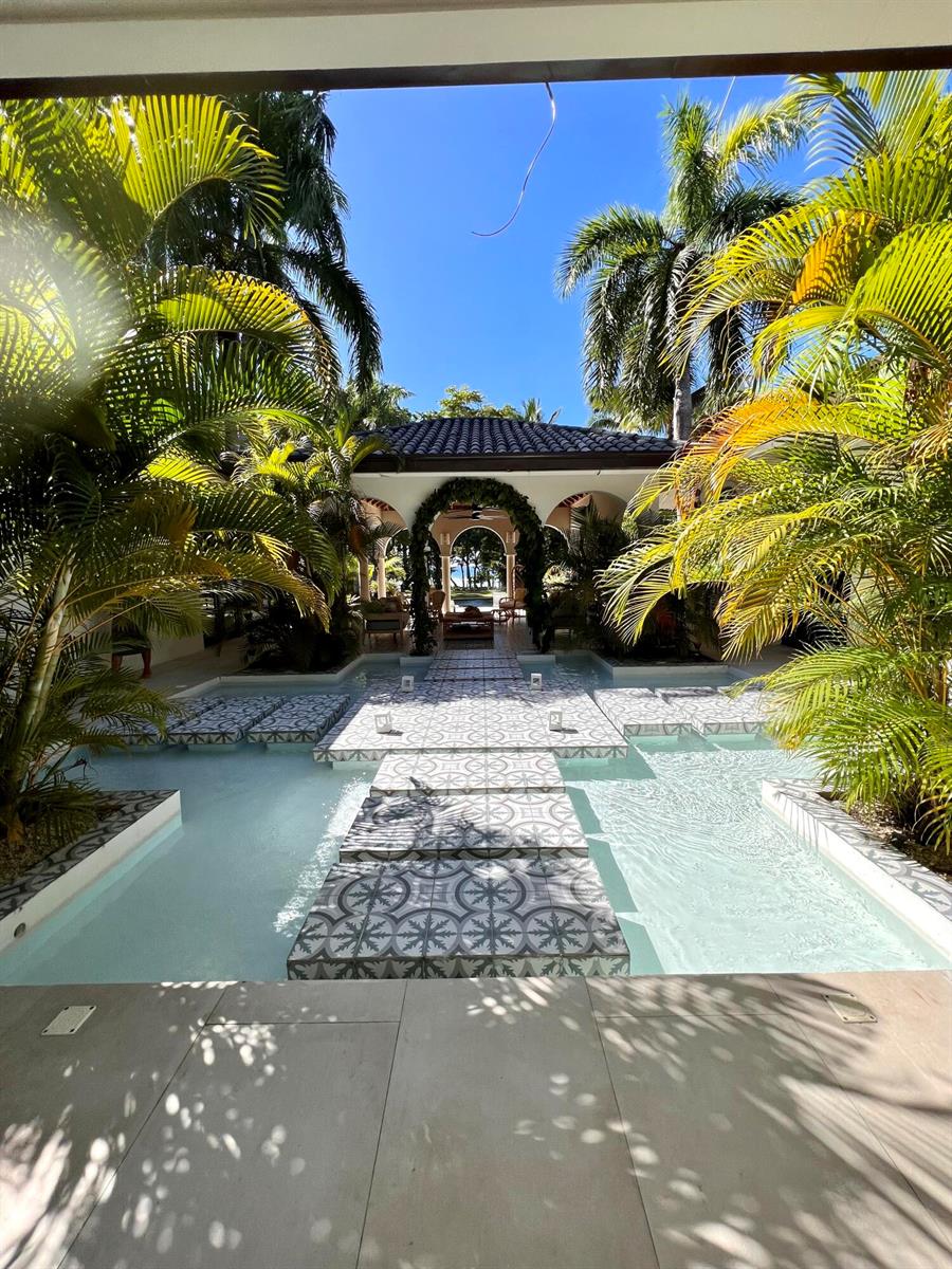 A courtyard features a decorative tiled walkway crossing a shallow pool surrounded by palm trees — 123456 Sea Horse Ranch Community, FL