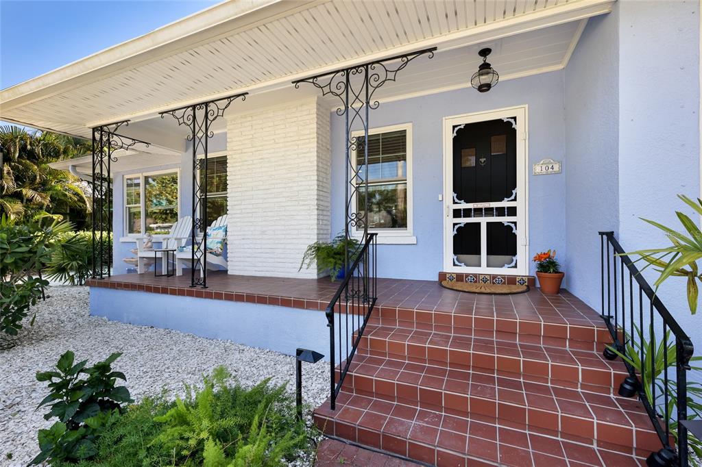 A blue house features a covered front porch with red tile steps and iron railings — 104 24TH STREET NW, BRADENTON, FL