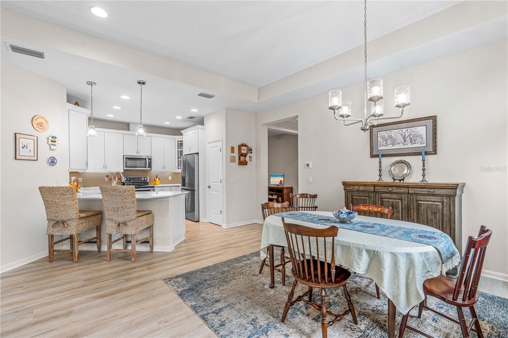 An open-concept dining area and kitchen with white cabinetry, wood-look flooring, and a chandelier — 466 MARGARITAVILLE AVENUE, DAYTONA BEACH, FL