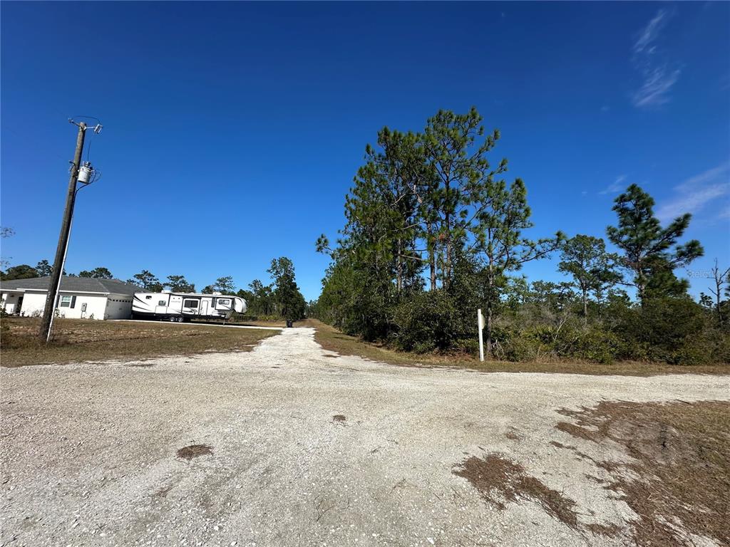 A gravel road leads past a white house and a parked RV toward trees — 22 BOUGAINVILLE DRIVE, INDIAN LAKE ESTATES, FL