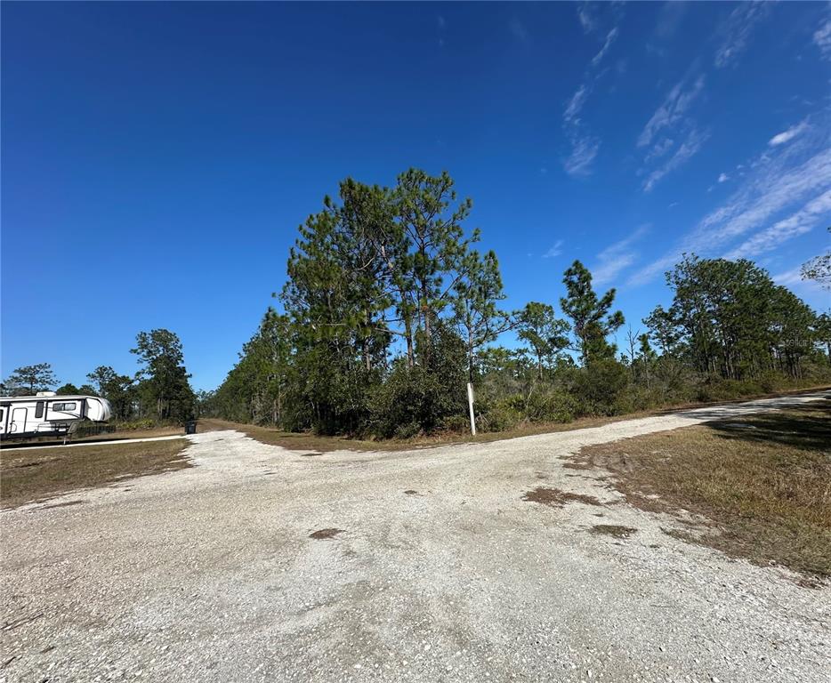 A gravel road forks in front of a wooded lot with a parked camper — 22 BOUGAINVILLE DRIVE, INDIAN LAKE ESTATES, FL