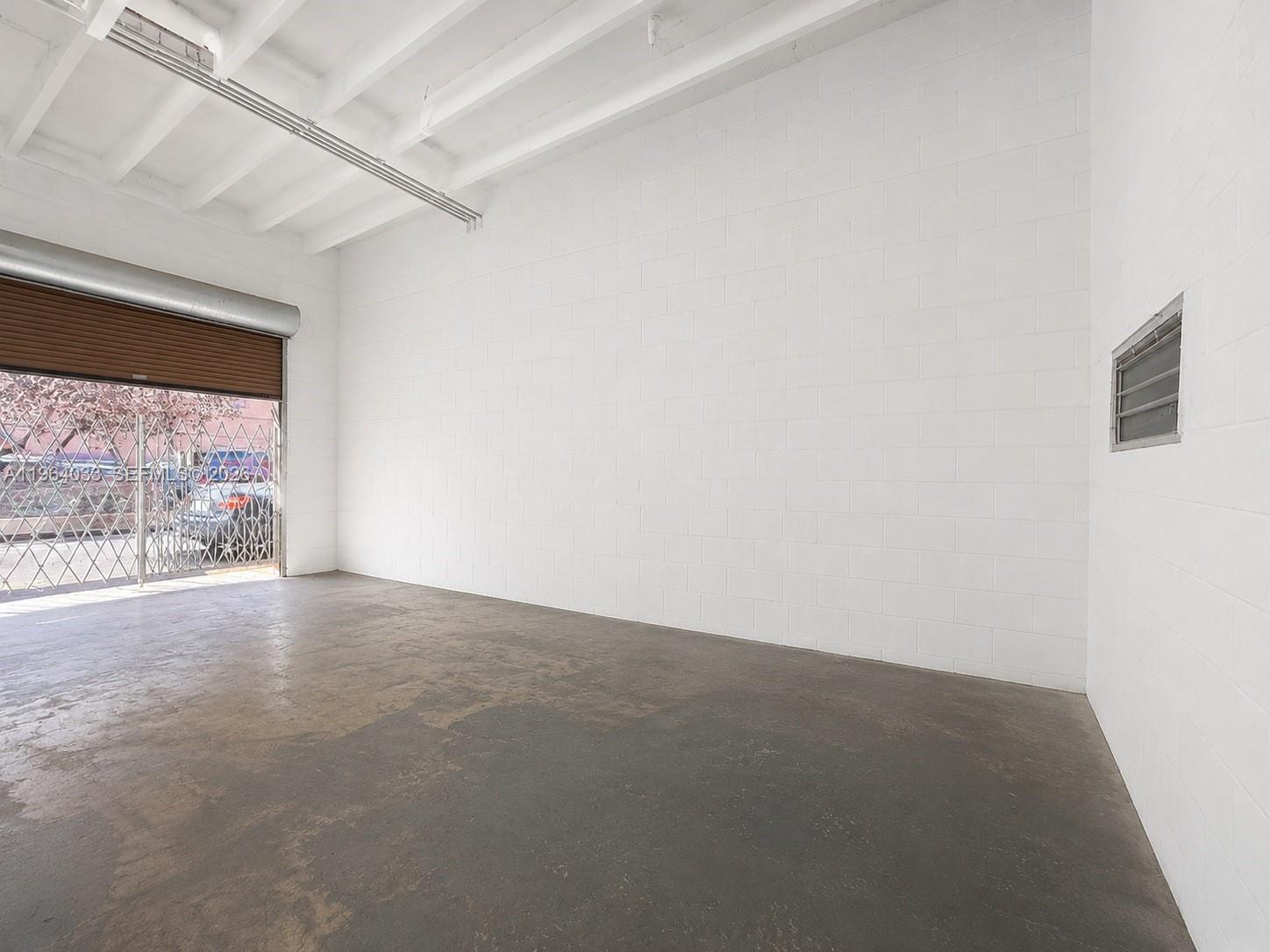 An empty industrial space features white concrete block walls, a concrete floor, and a roll-up door — 13690 SW 142nd Ave # A, Miami FL 33186, MIAMI, FL