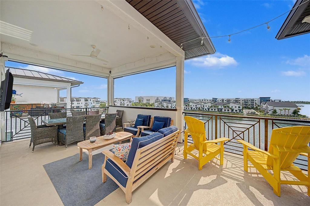 A covered outdoor balcony features wicker dining furniture, lounge seating, and yellow chairs overlooking water — 5351 BRIDGE STREET UNIT 38, TAMPA, FL