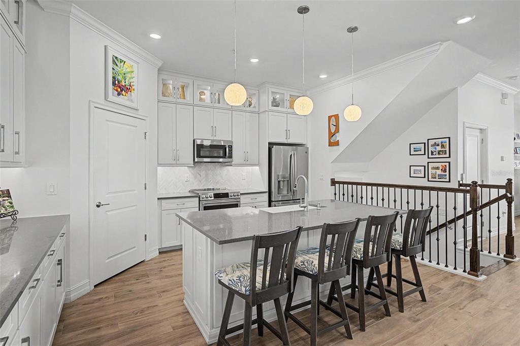 A modern white kitchen features a large gray island with four bar stools and wood flooring — 5351 BRIDGE STREET UNIT 38, TAMPA, FL