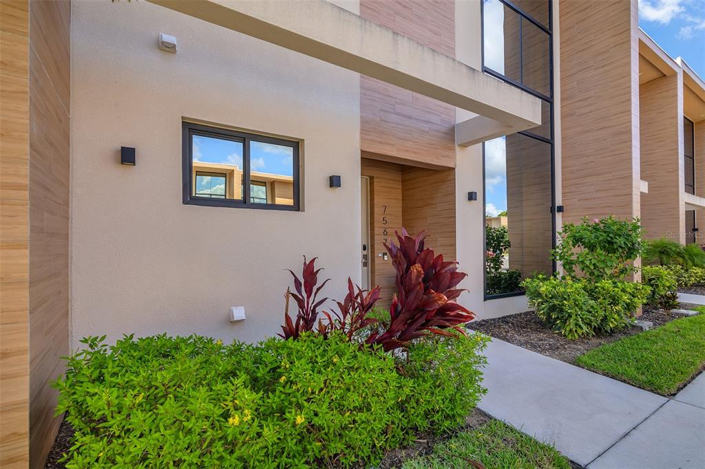 The exterior of a modern townhouse features wood-look siding, a beige wall, and landscaping — 7567 BROOKLYN DRIVE, KISSIMMEE, FL