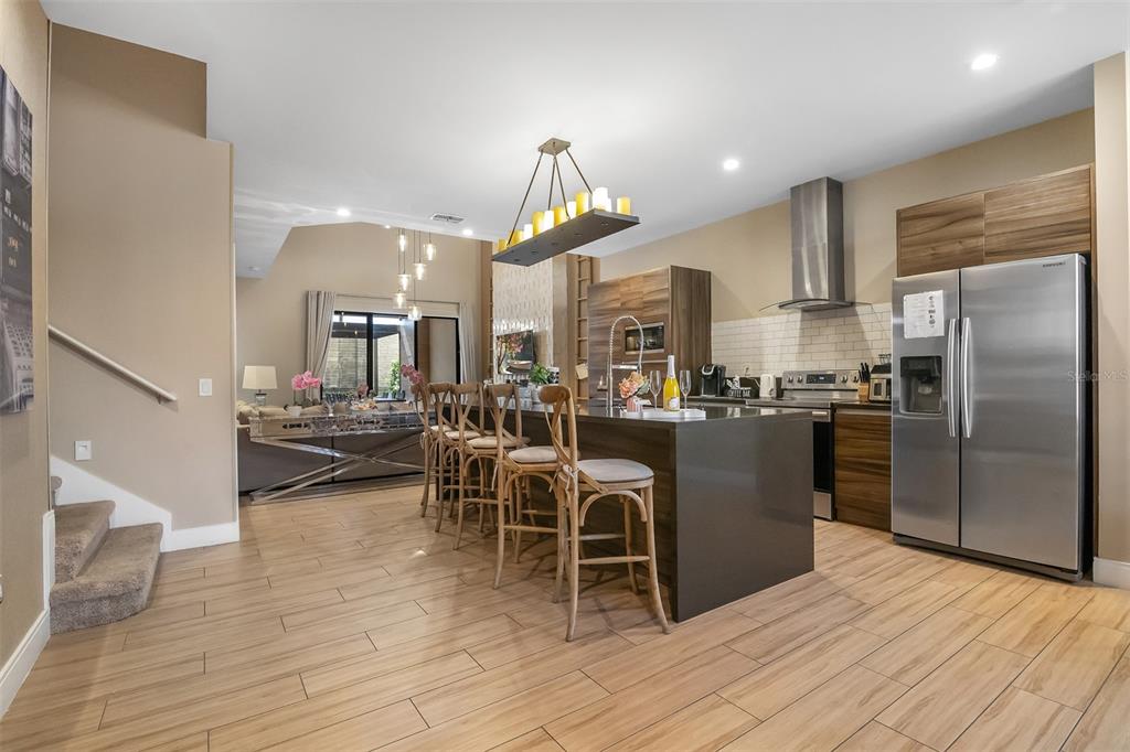A modern kitchen features a large island with bar seating, wood cabinetry, and stainless appliances — 7567 BROOKLYN DRIVE, KISSIMMEE, FL
