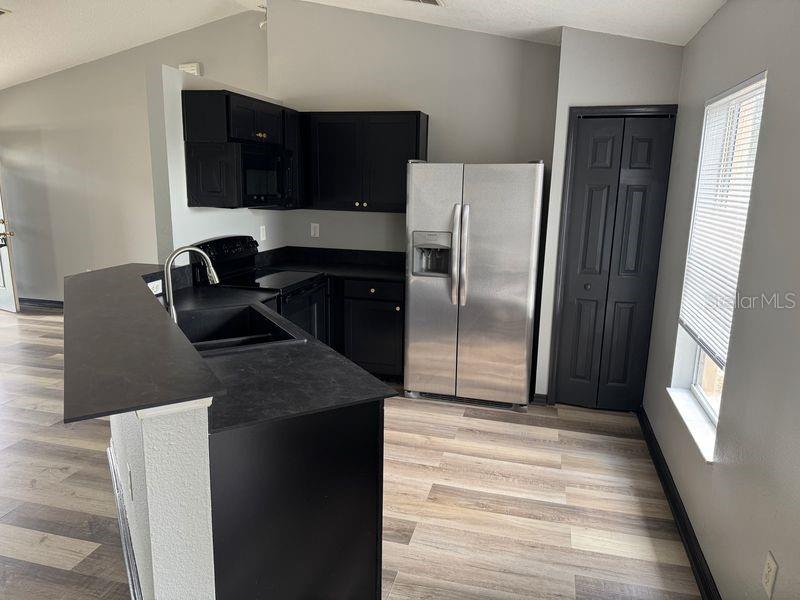 A kitchen features black cabinets, dark countertops, stainless steel appliances, and light wood-look flooring — 6289 MARINER BOULEVARD, SPRING HILL, FL