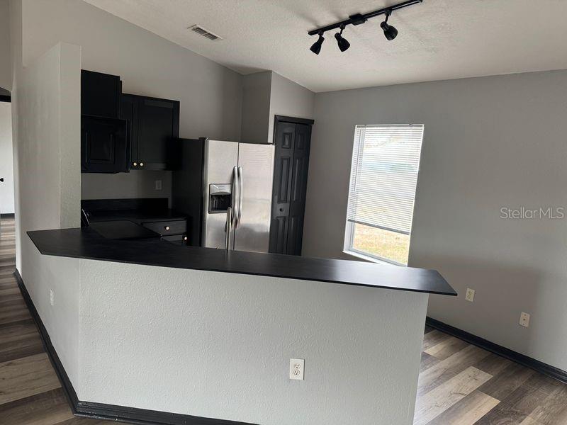A kitchen features a black breakfast bar, dark cabinetry, stainless steel appliances, and wood-look flooring — 6289 MARINER BOULEVARD, SPRING HILL, FL