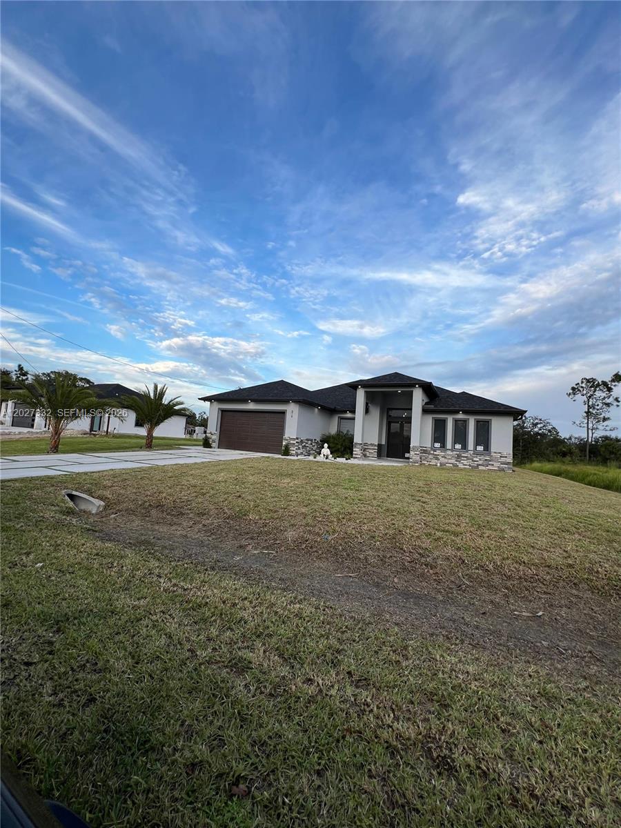 A modern single-story house with a dark roof and stone accents sits on a lawn — 616 Maple Ave N, Lehigh Acres FL 33972, LEHIGH ACRES, FL
