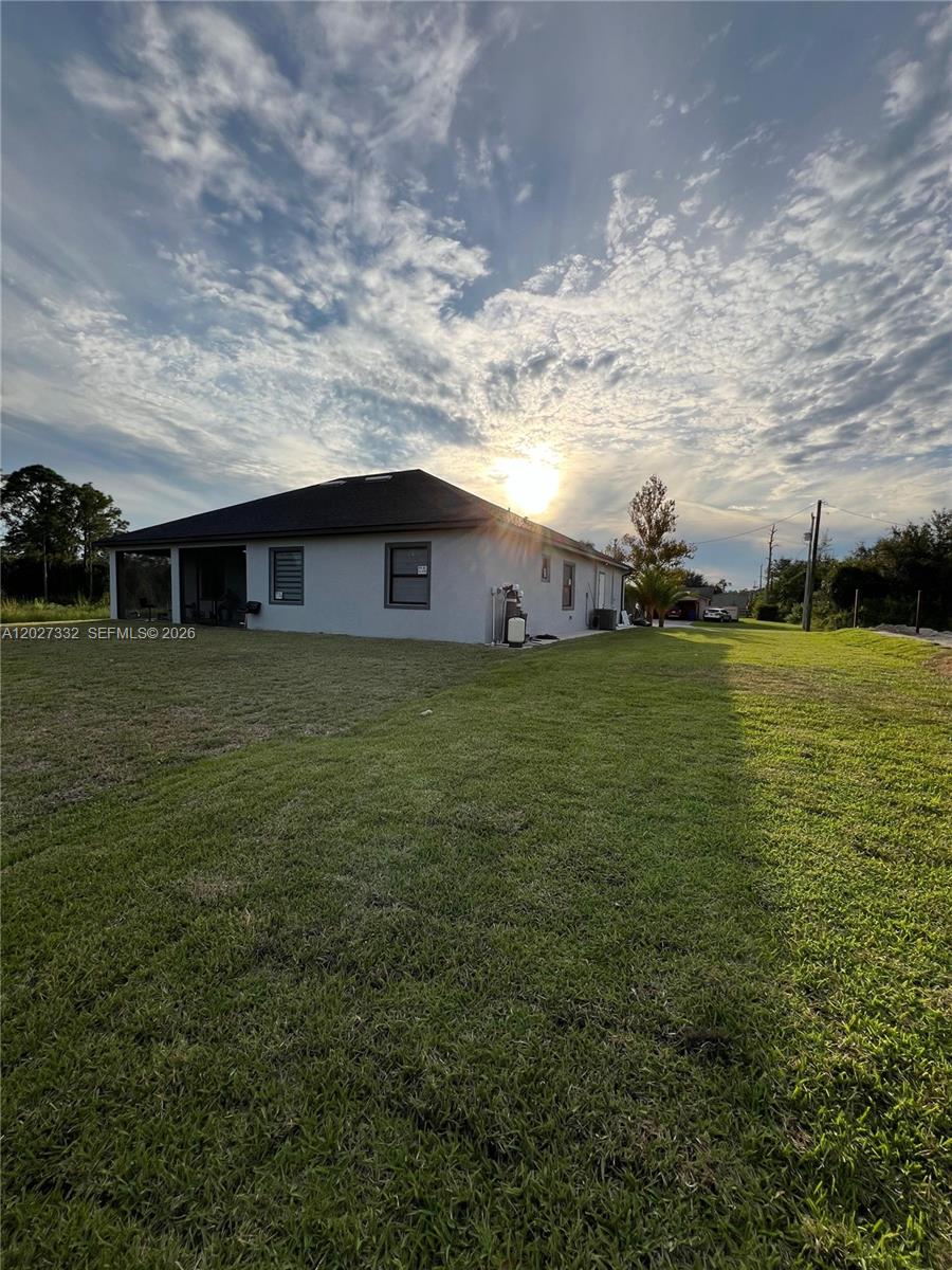 The exterior of a single-story house with a large backyard under a cloudy sky — 616 Maple Ave N, Lehigh Acres FL 33972, LEHIGH ACRES, FL