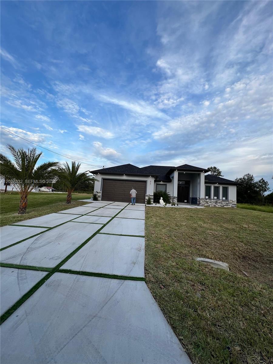 A modern single-story house with a concrete driveway and palm trees under a cloudy sky — 616 Maple Ave N, Lehigh Acres FL 33972, LEHIGH ACRES, FL