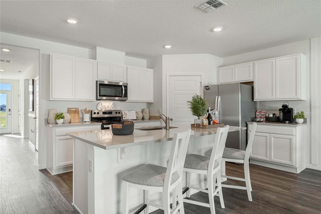 A modern kitchen features white cabinetry, stainless steel appliances, a central island, and wood-look flooring — 2759 ADELINE AVENUE, WINTER HAVEN, FL