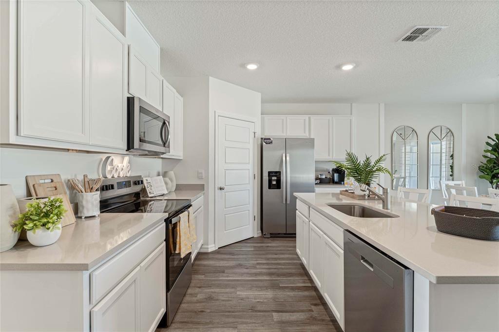 A modern kitchen features white cabinets, stainless steel appliances, a center island, and wood-look flooring — 2759 ADELINE AVENUE, WINTER HAVEN, FL
