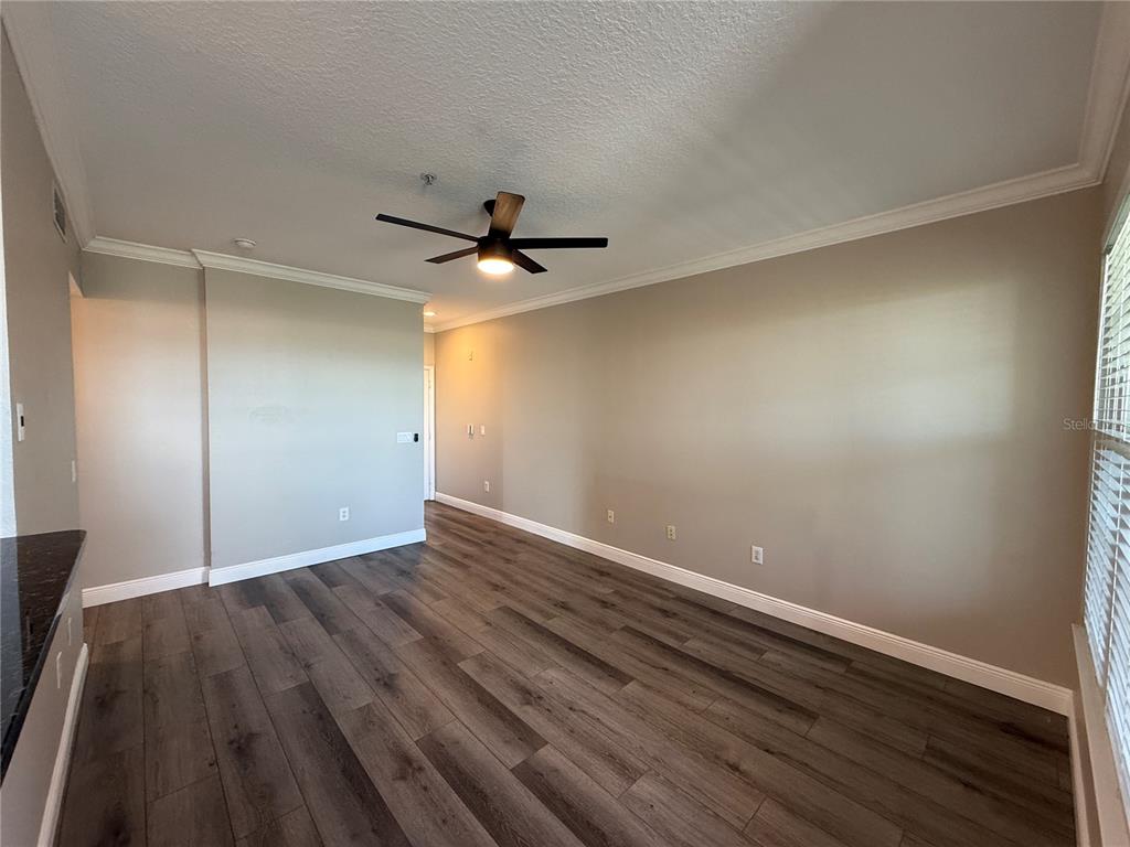 An empty room features wood-look flooring, beige walls, a ceiling fan, and crown molding — 1910 E PALM AVENUE UNIT 11321, TAMPA, FL