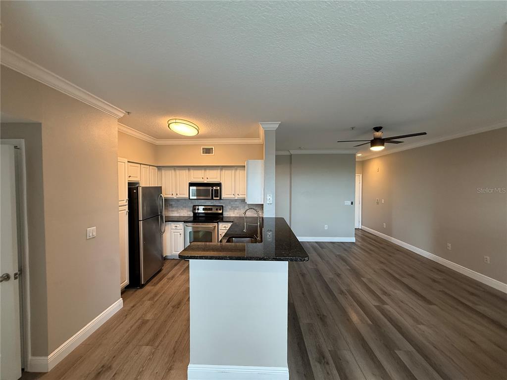 An open-concept kitchen with white cabinets, stainless steel appliances, and dark countertops overlooks a living area — 1910 E PALM AVENUE UNIT 11321, TAMPA, FL