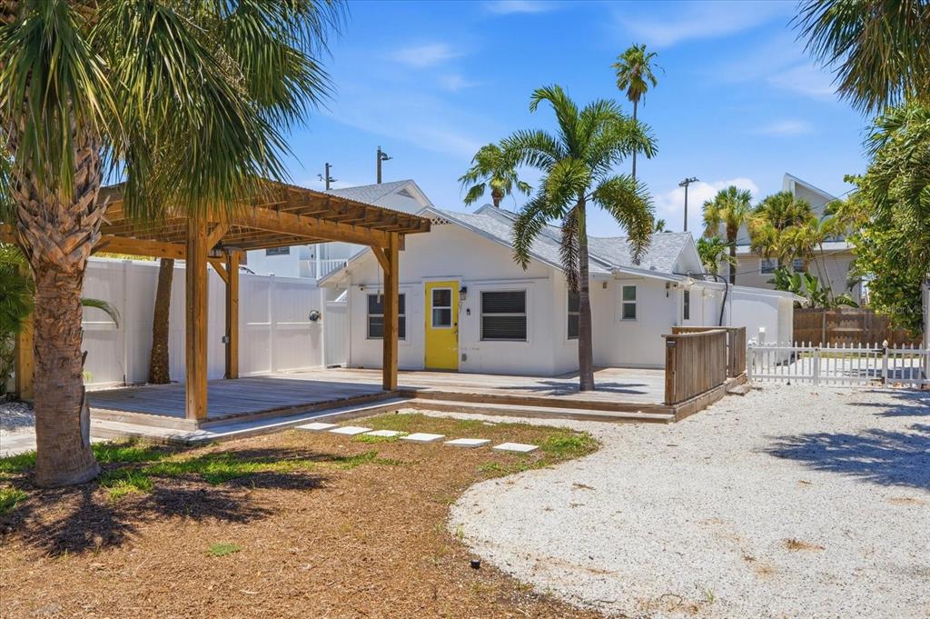 A white house with a yellow door features a wooden pergola and deck in front — 107 14TH AVENUE, ST PETE BEACH, FL