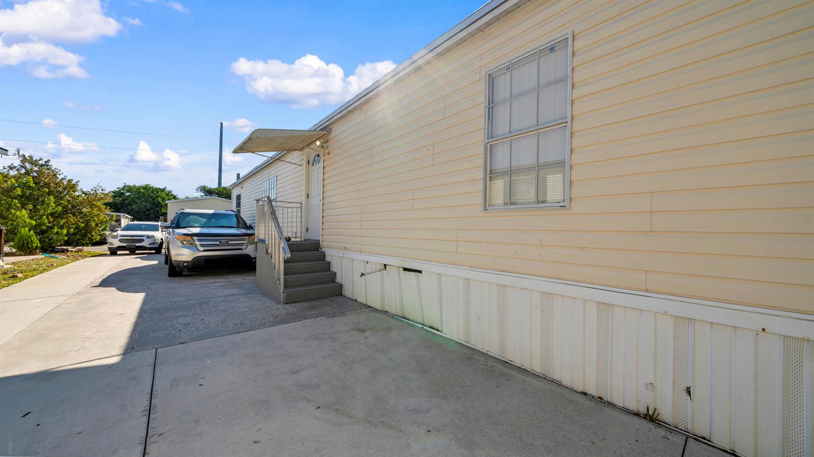 The exterior of a light-colored mobile home features a concrete driveway and metal stairs — 4905 NE 2nd Way, Pompano Beach FL 33064, POMPANO BEACH, FL