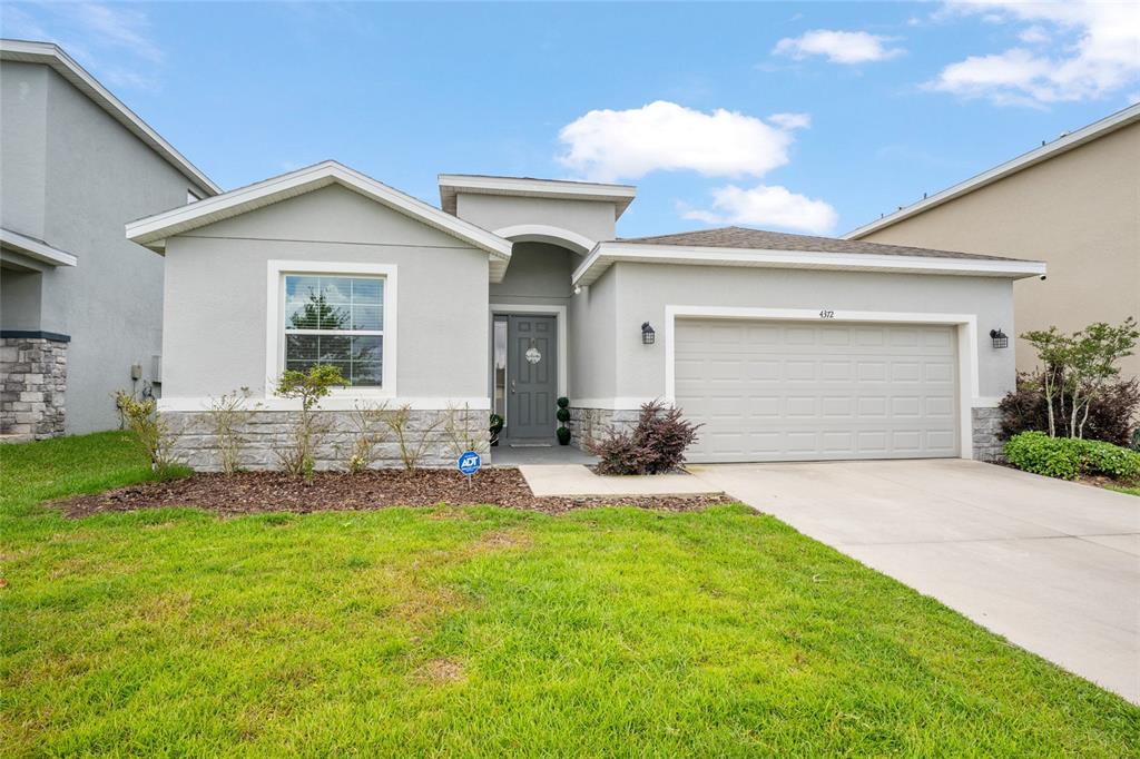 A single-story house features a gray stucco exterior, stone accents, and an attached two-car garage — 4372 SW 56TH PLACE, OCALA, FL